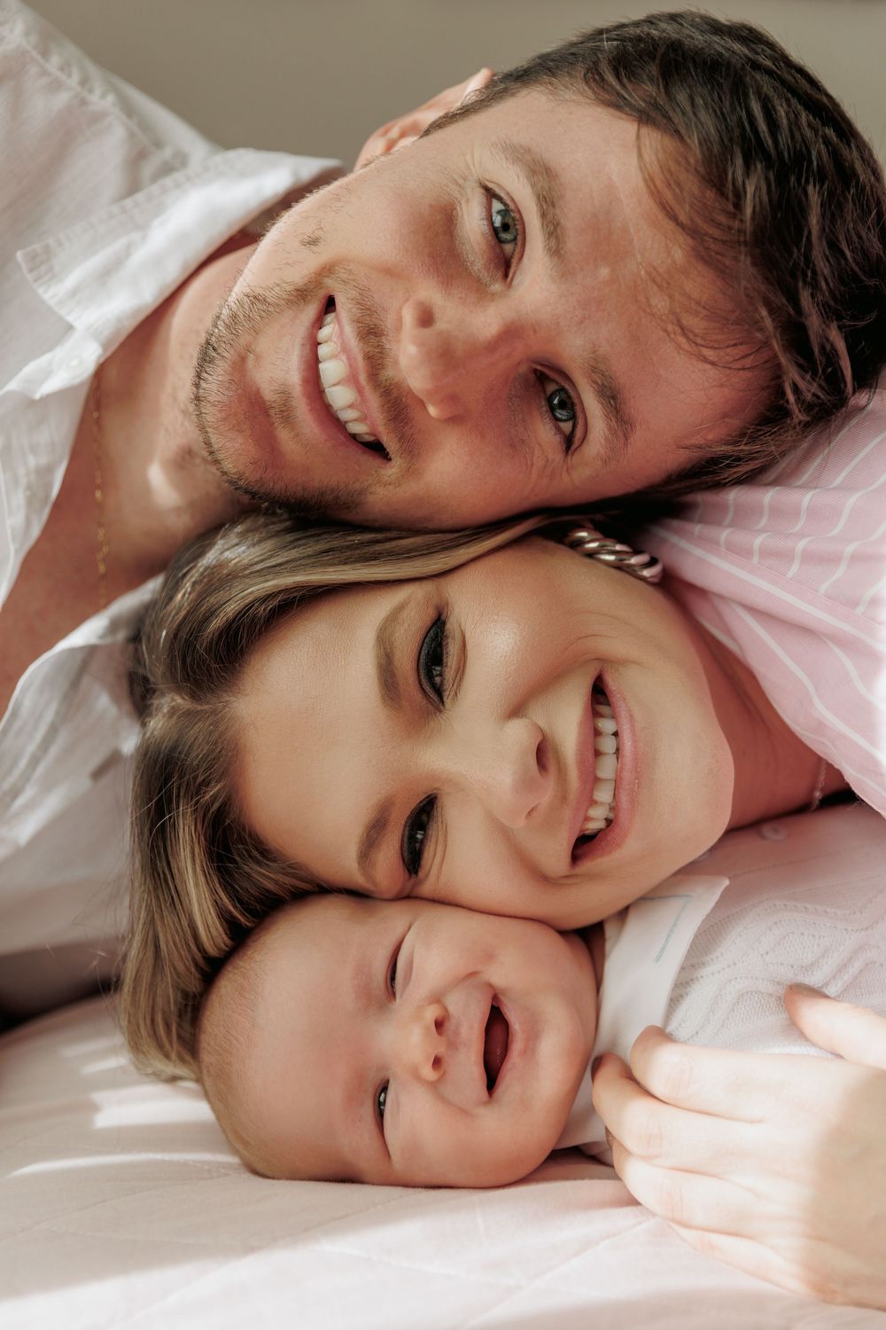 Smiling family laying together on white bedding in close-up portrait showing joy and connection.