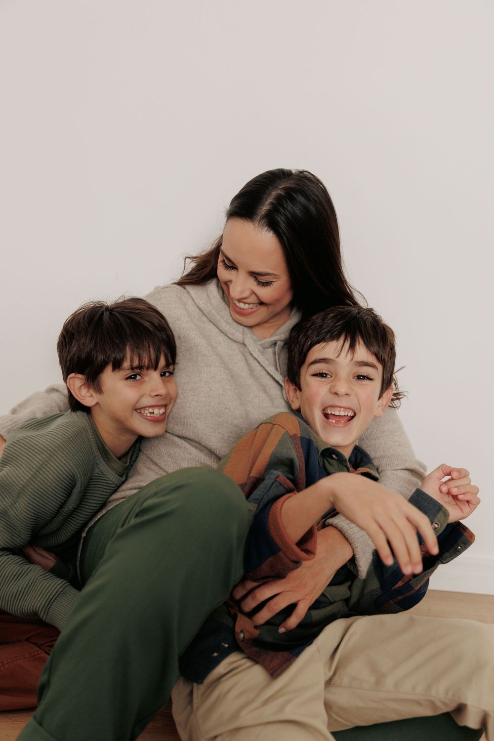 Family shares joyful moment cuddling and laughing together on floor in casual indoor setting.