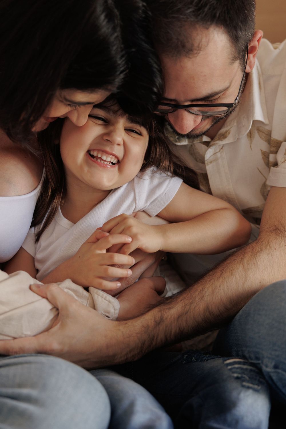 Candid sequence shows playful tickling moment between parent and child laughing together on couch.