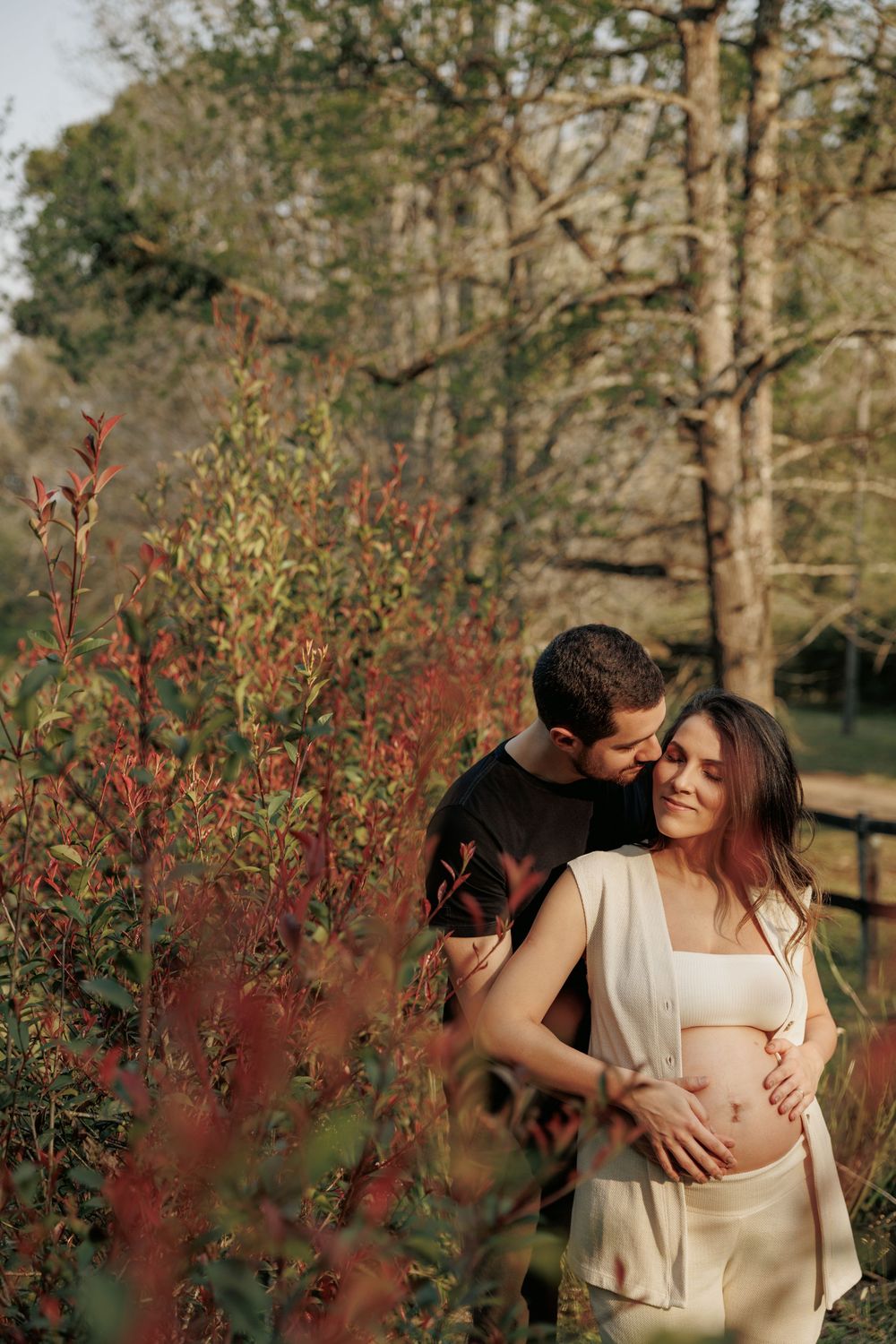 A couple shares an intimate moment among autumn foliage in a golden-hour outdoor setting.