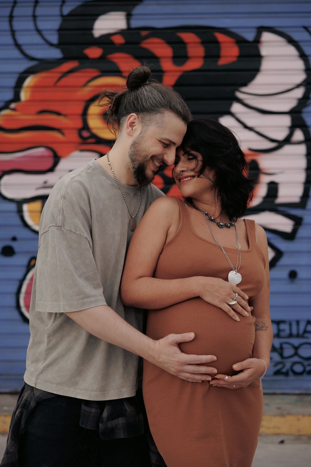 A tender maternity photo against vibrant street art as an expecting couple shares an intimate moment.