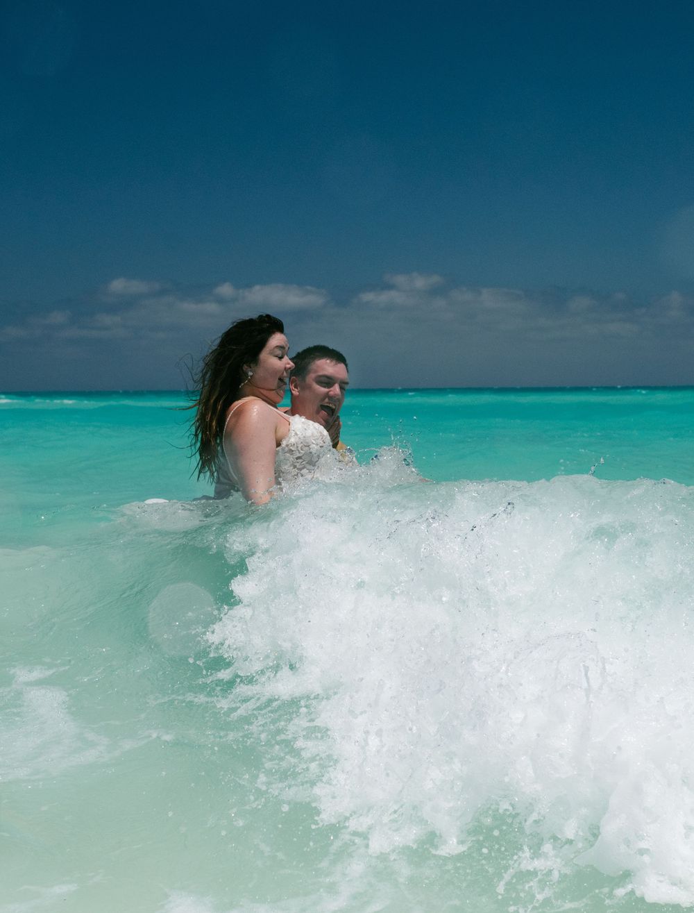 A couple embraces in the turquoise ocean waves during their beach wedding photoshoot.