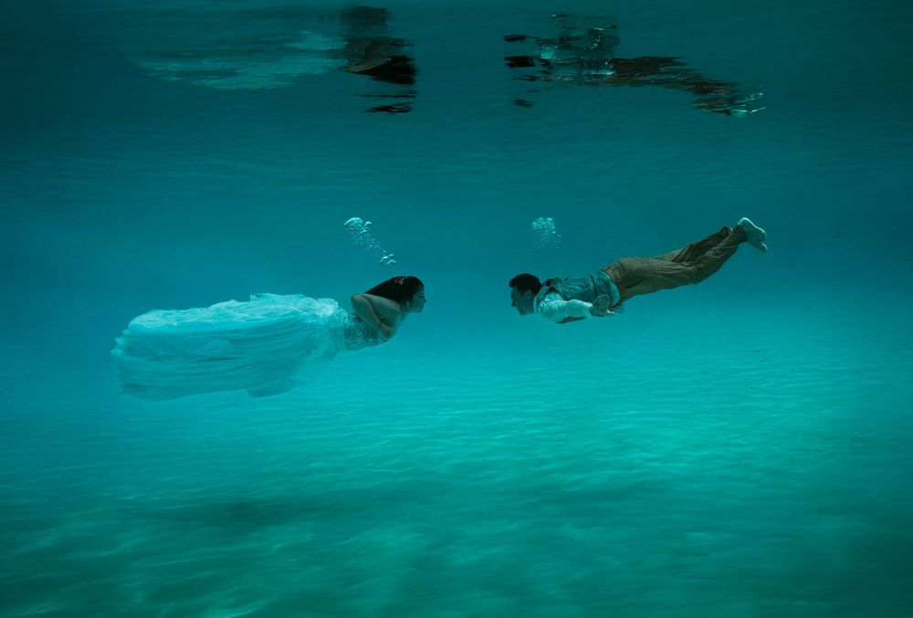 People swimming underwater in clear turquoise ocean water.