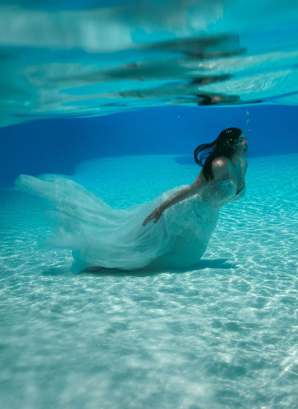 Underwater view of flowing white fabric against sandy ocean floor.