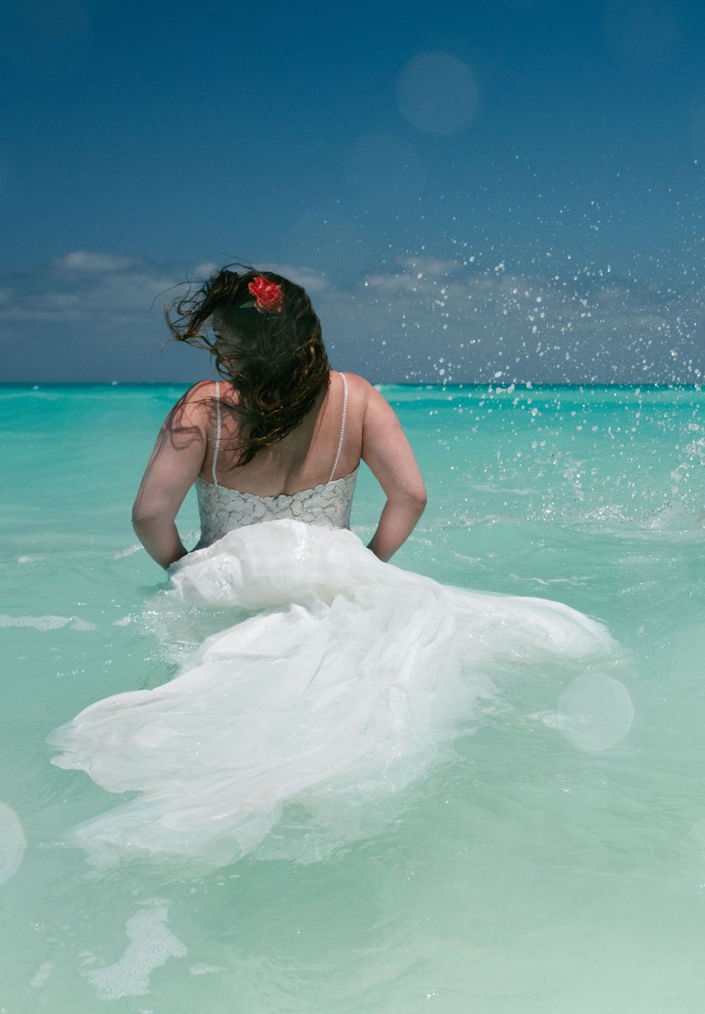 A bride splashes in turquoise ocean waters wearing a flowing white wedding dress.