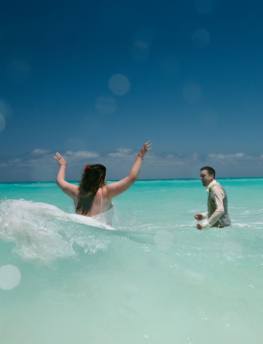 A playful moment captured as a couple enjoys the crystal clear waters during their beach wedding.