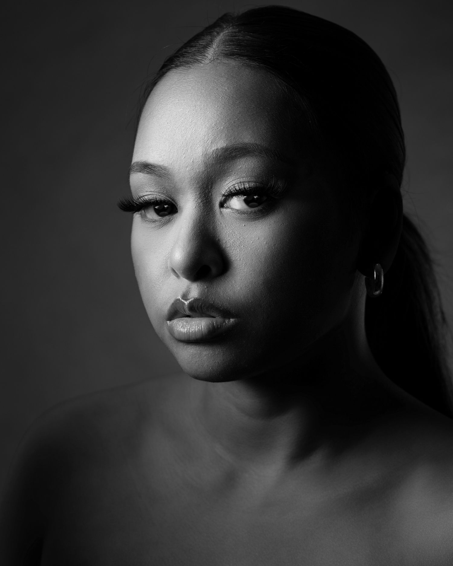 Dramatic black and white portrait photograph showing a profile view against dark background with soft, moody lighting.