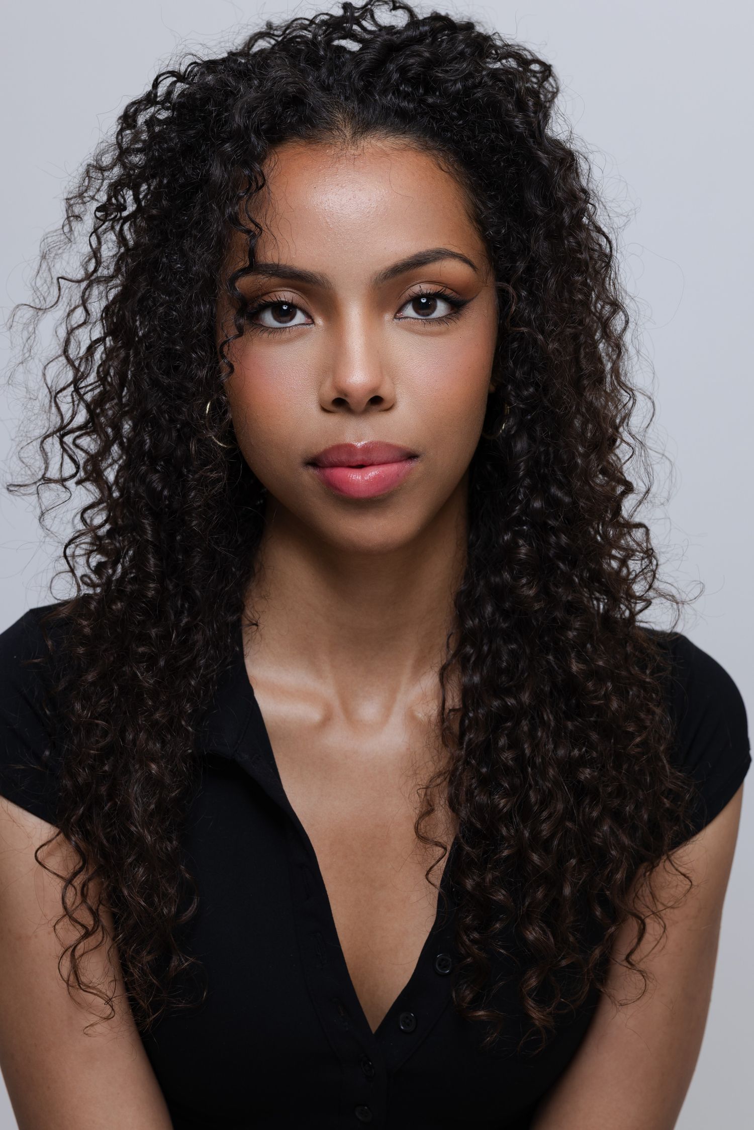 Professional studio portrait featuring long curly natural hair and elegant black v-neck top against light grey background in Mississauga
