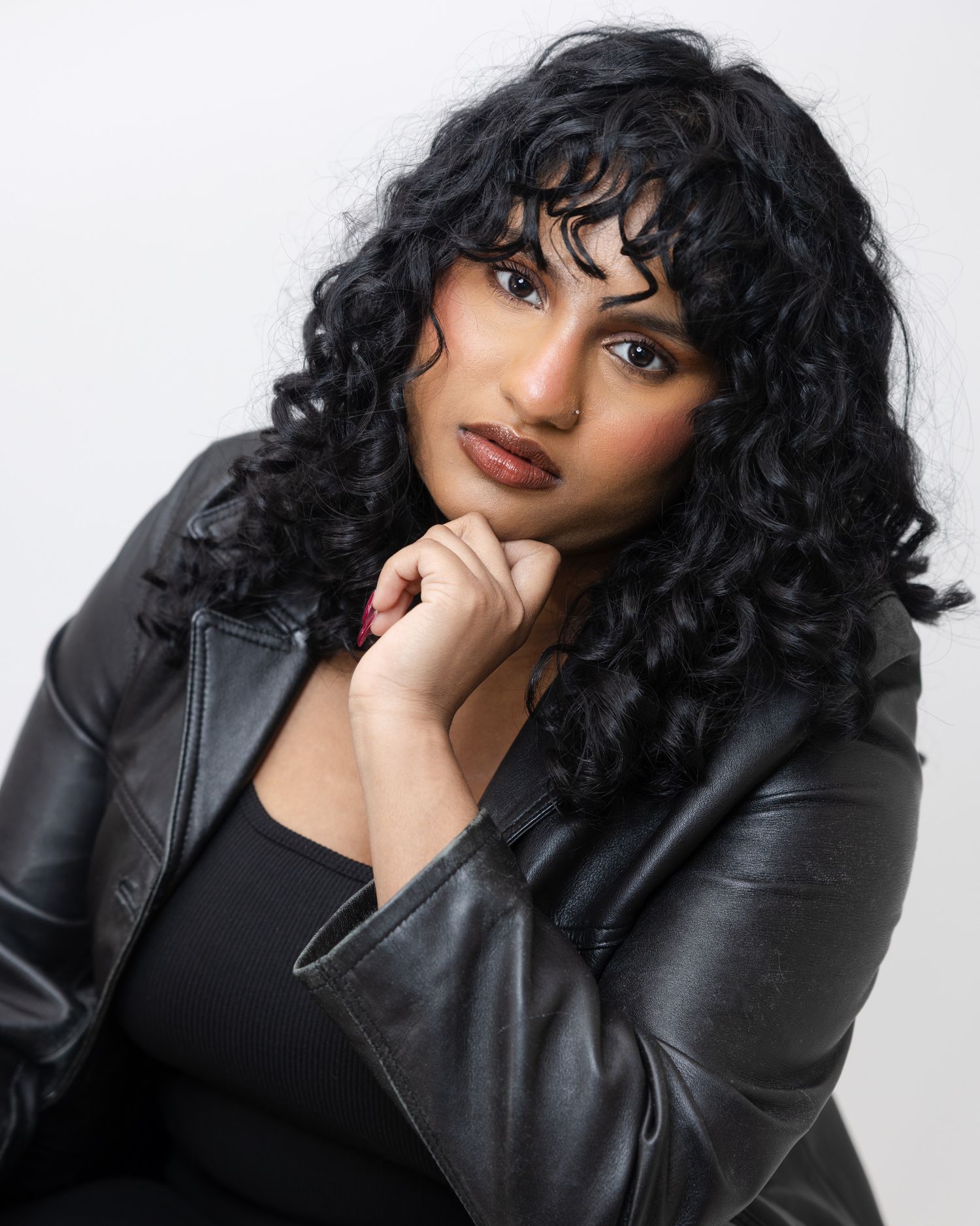 A portrait of a model wearing black leather jacket and curly dark hair against white background.