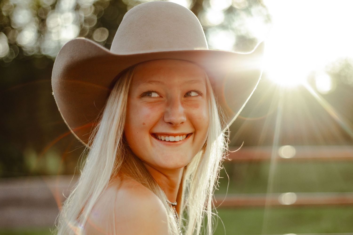 Person smiling at sunset in a natural garden setting with warm golden sunlight filtering through leaves and trees.