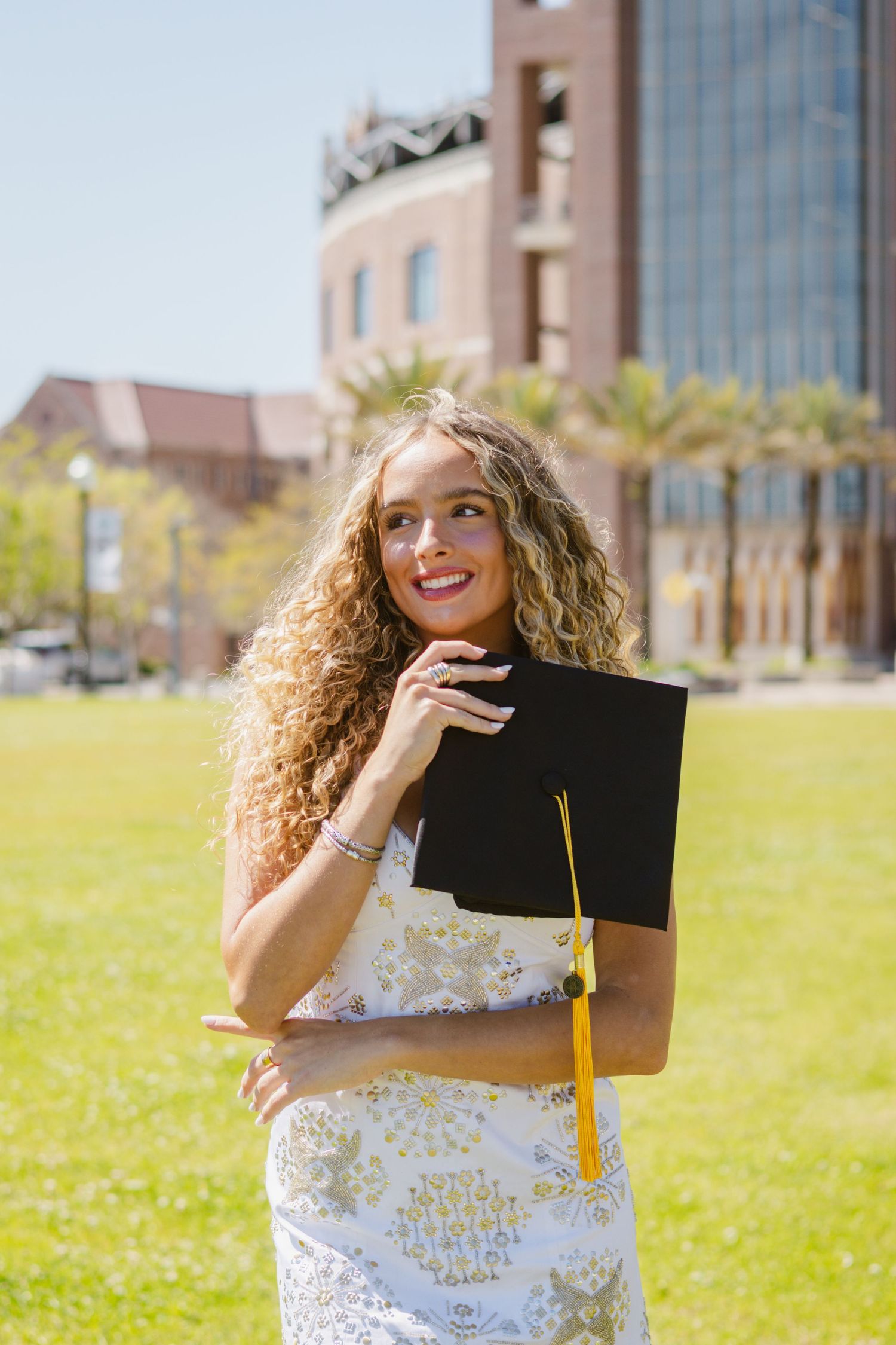 A girl smiling with her graduation cap tucked under her chin on Langford green at Florida State University.