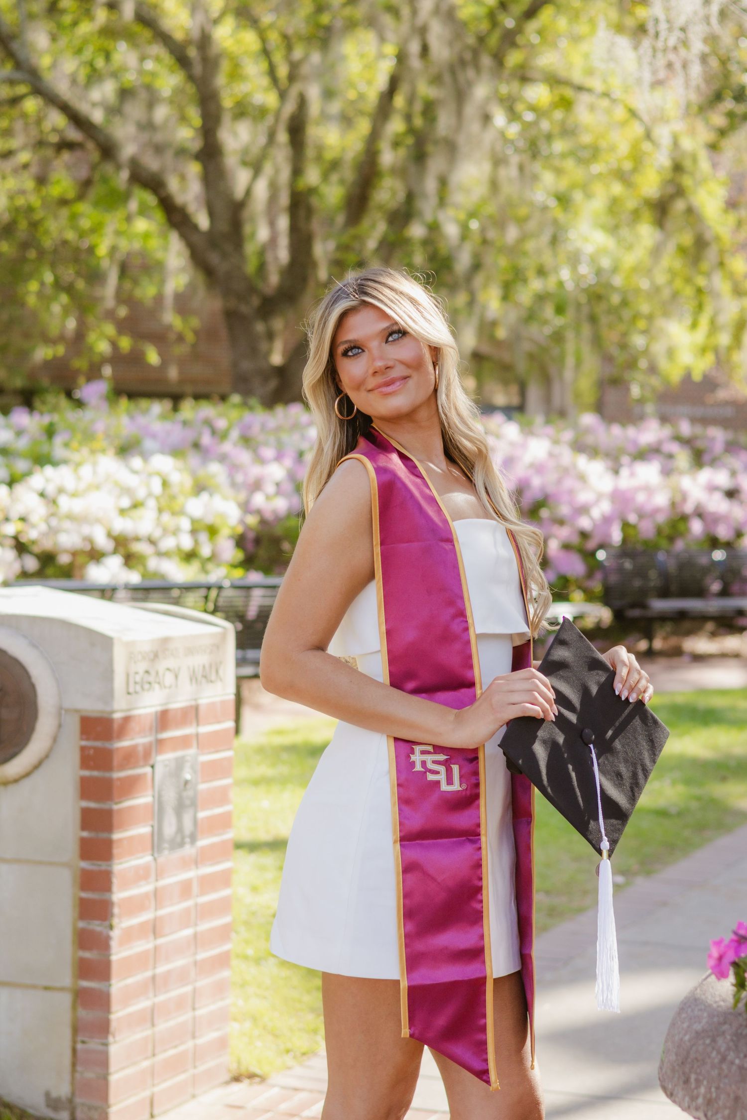 Wearing a stole and holding her graduation cap, a proud FSU graduate is looking over her shoulder at the Westcott fountain.