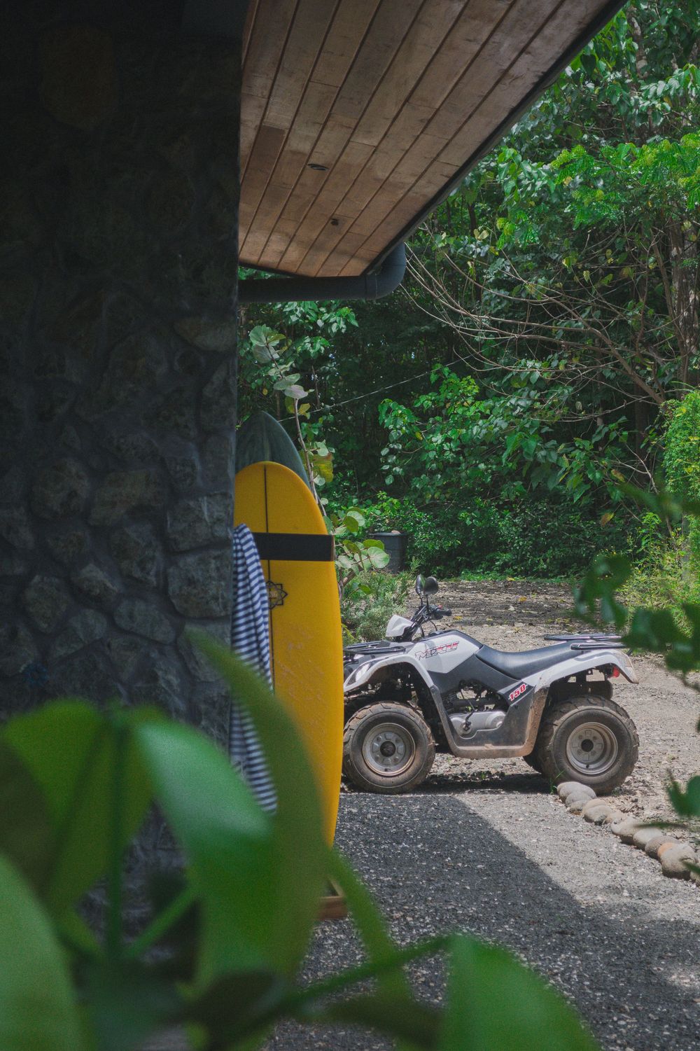 A yellow surfboard and ATV parked outside a rustic cabin surrounded by lush greenery.