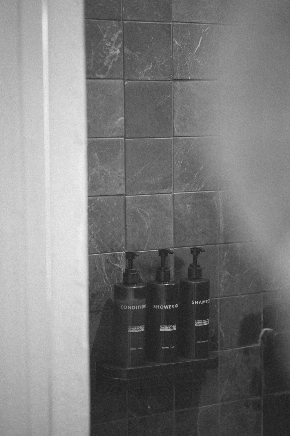 Black pump bottles arranged on dark tile shower shelf in monochromatic bathroom.