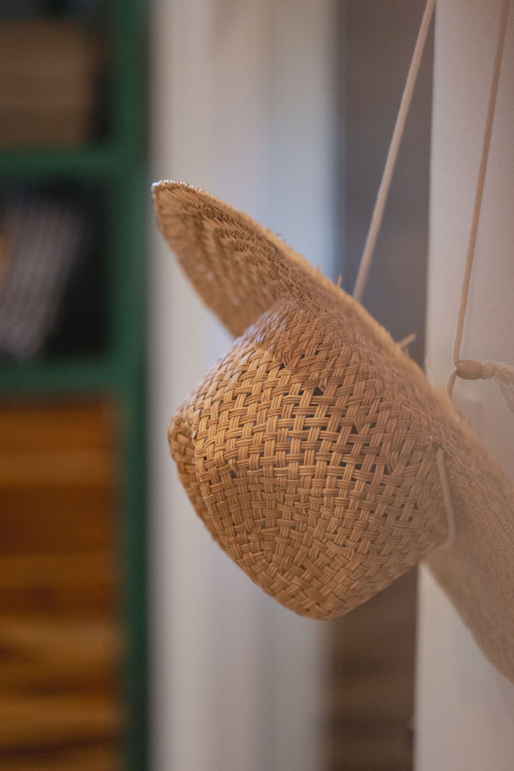 Woven straw sun hat hanging on white wall peg.