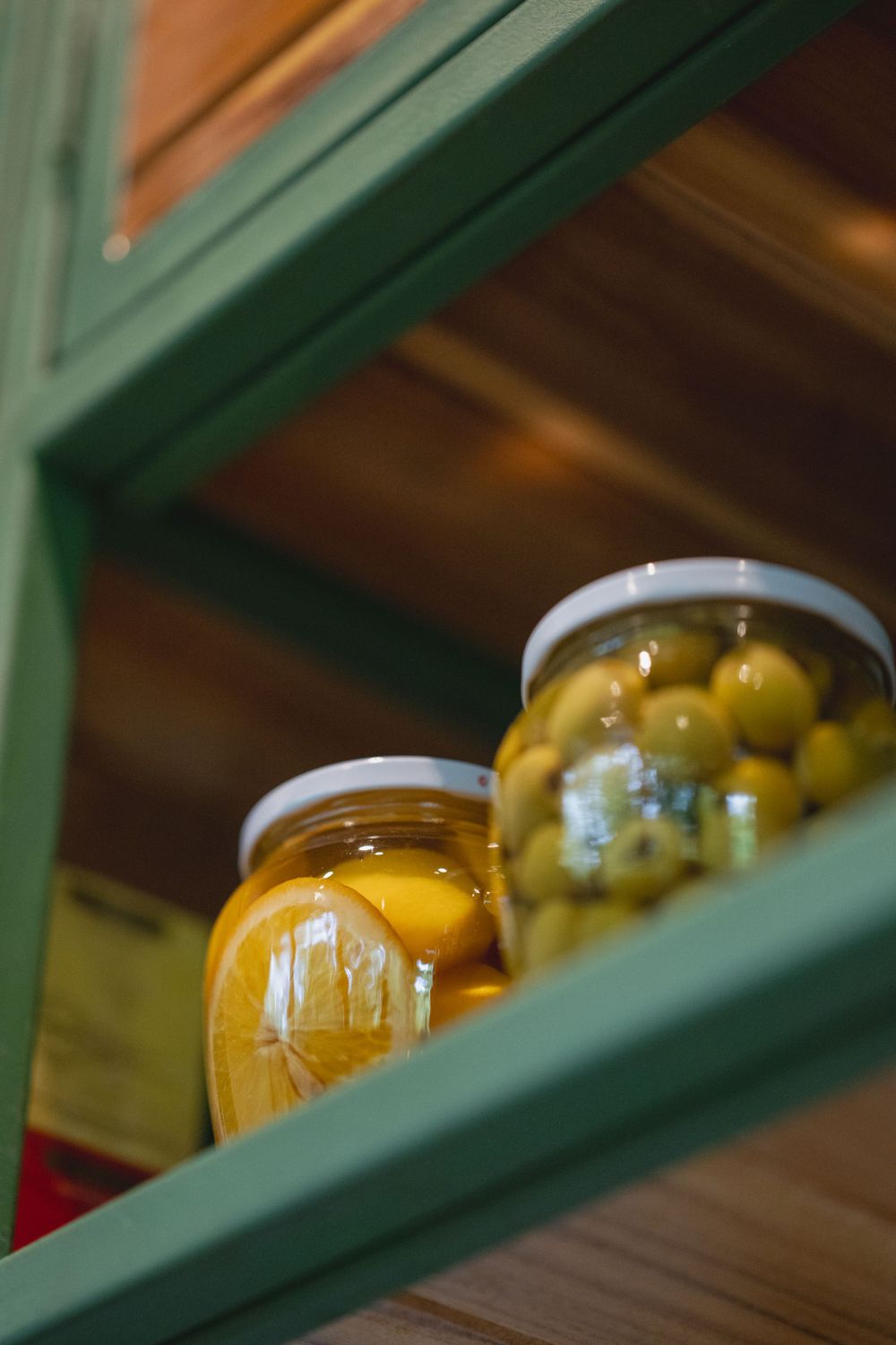 Glass jars filled with preserved yellow fruits on green shelving.