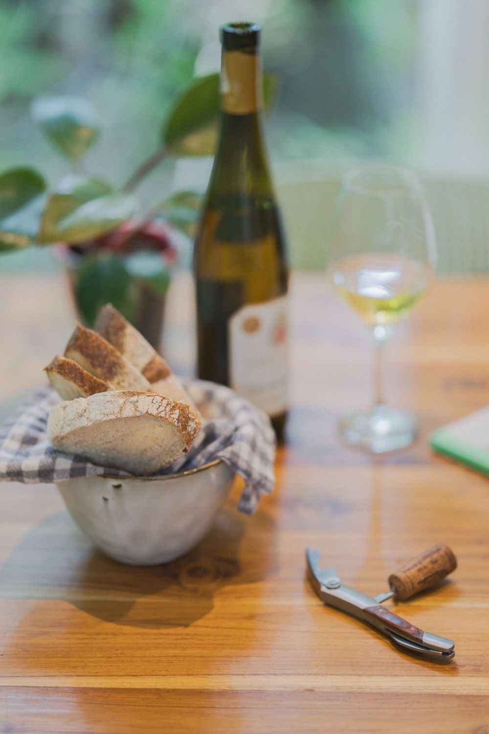 Rustic table setting with sliced bread, wine bottle, and corkscrew.