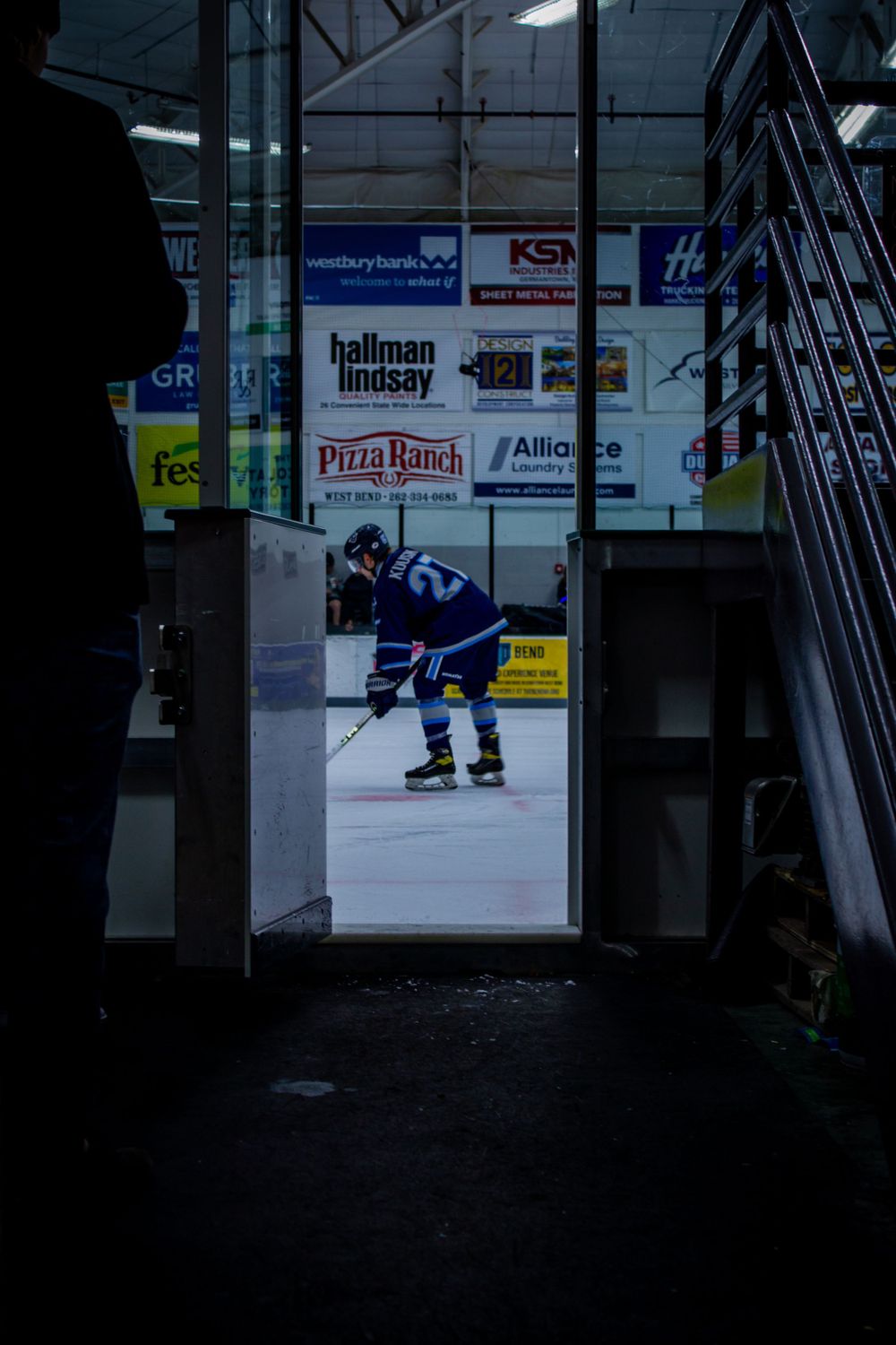 View through doorway shows hockey player on ice with advertising boards visible in background.
