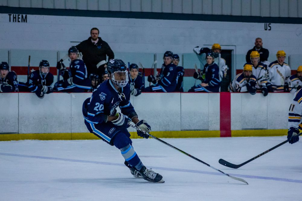 Hockey player in blue uniform skating with puck during competitive match.