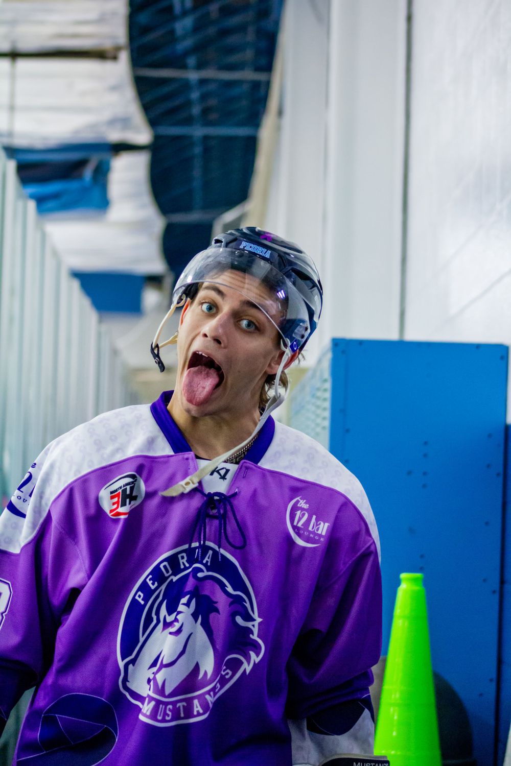 Hockey player Blake Mitchell in purple jersey with peoria mustangs logo making playful expression before a game.