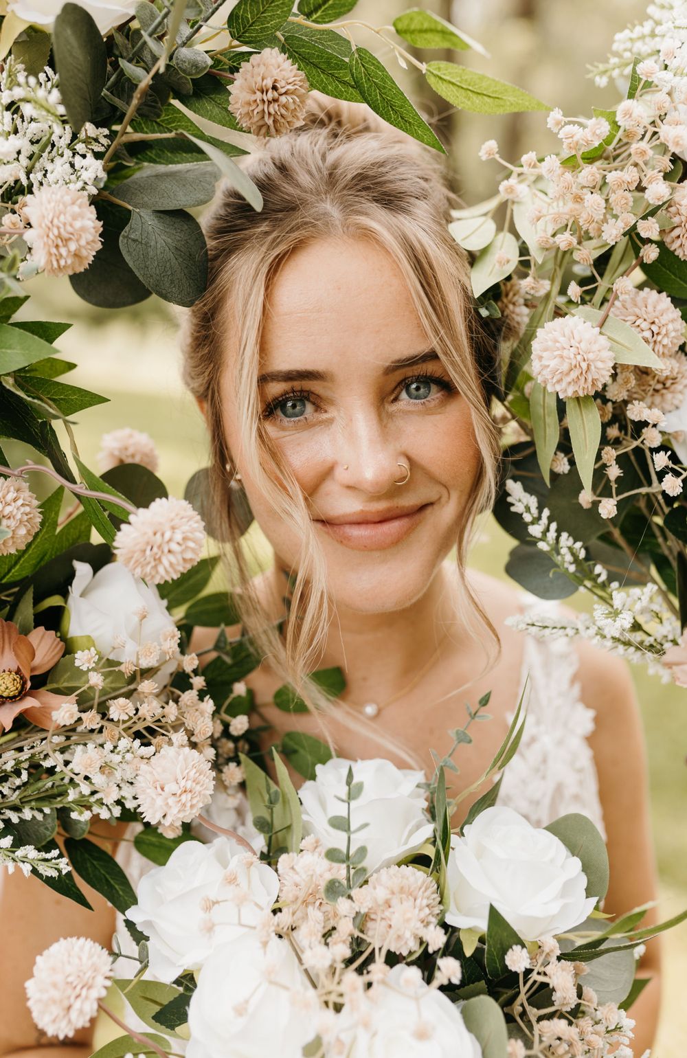 Close-up portrait of smiling bride with blue eyes surrounded by white and blush floral bouquet.
