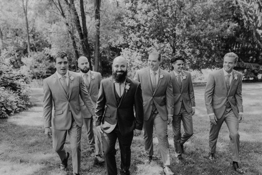 Black and white photo of groom leading groomsmen walking confidently through garden.
