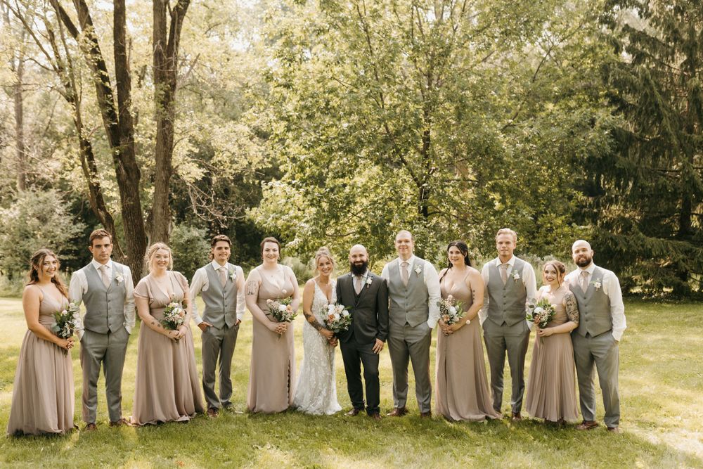 Bride and groom with full wedding party in blush and gray attire posing in garden.