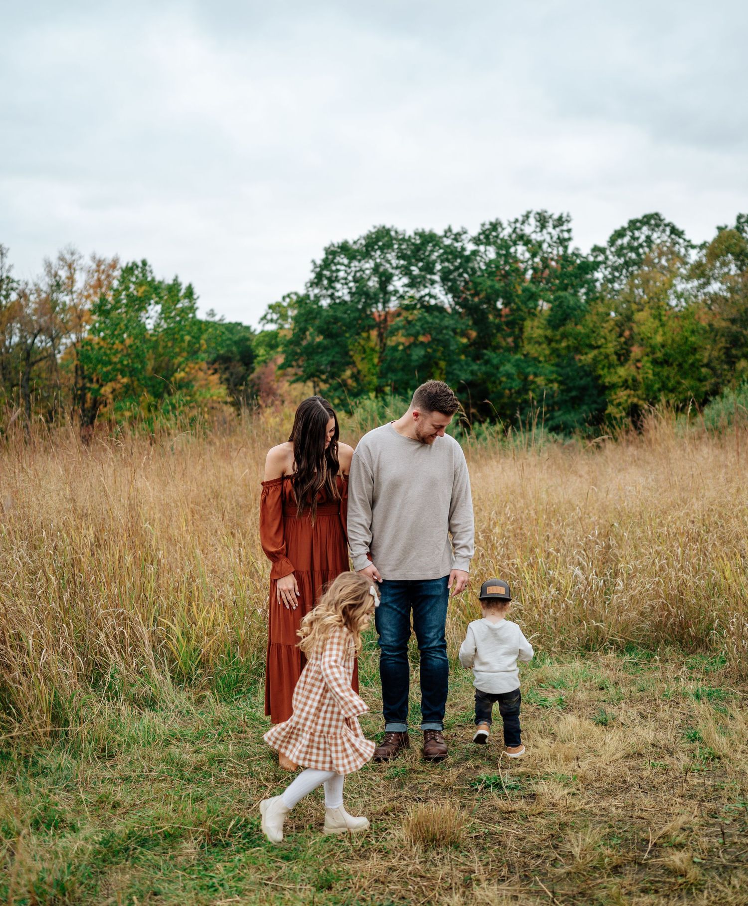 Family walking together through tall autumn grass in a natural field setting.