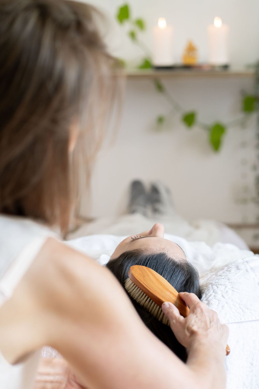 Hair brushing treatment being performed in serene spa setting with decorative vines and candles.