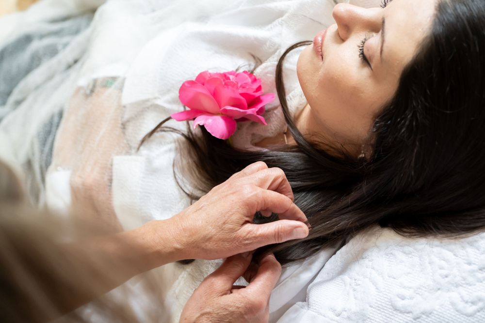 A person lying down with a pink rose on a white pillow during a relaxation treatment.