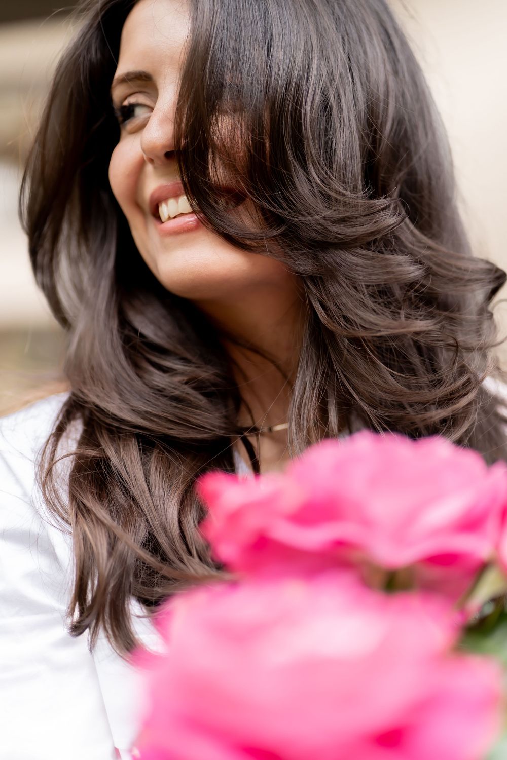 Dark wavy hair styled with soft layers against pink flowers in foreground.