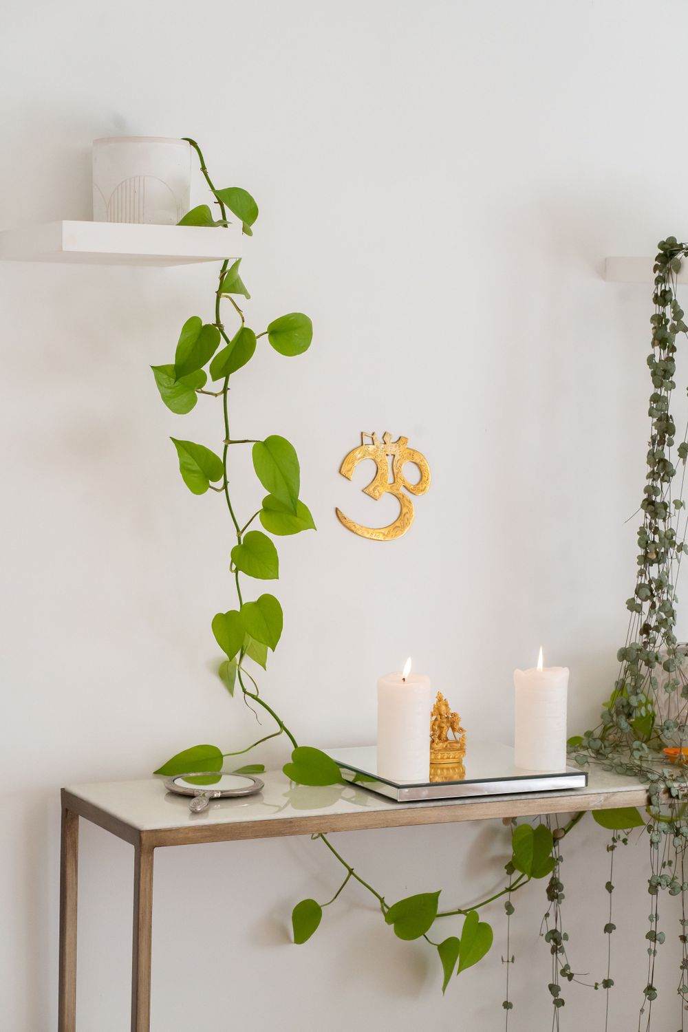 Minimalist spa decor featuring climbing plants, white candles, and a golden Om symbol on the wall.
