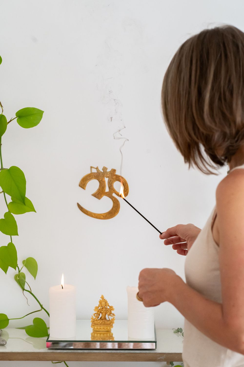 Person lighting incense near spiritual altar with Om symbol and green plants.