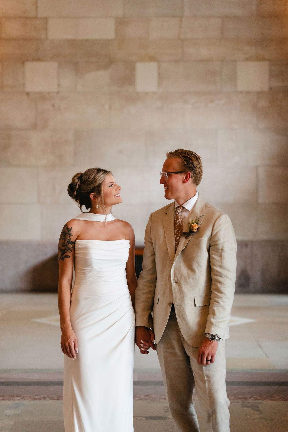 A couple shares a joyful moment together in formal attire against a stone wall.