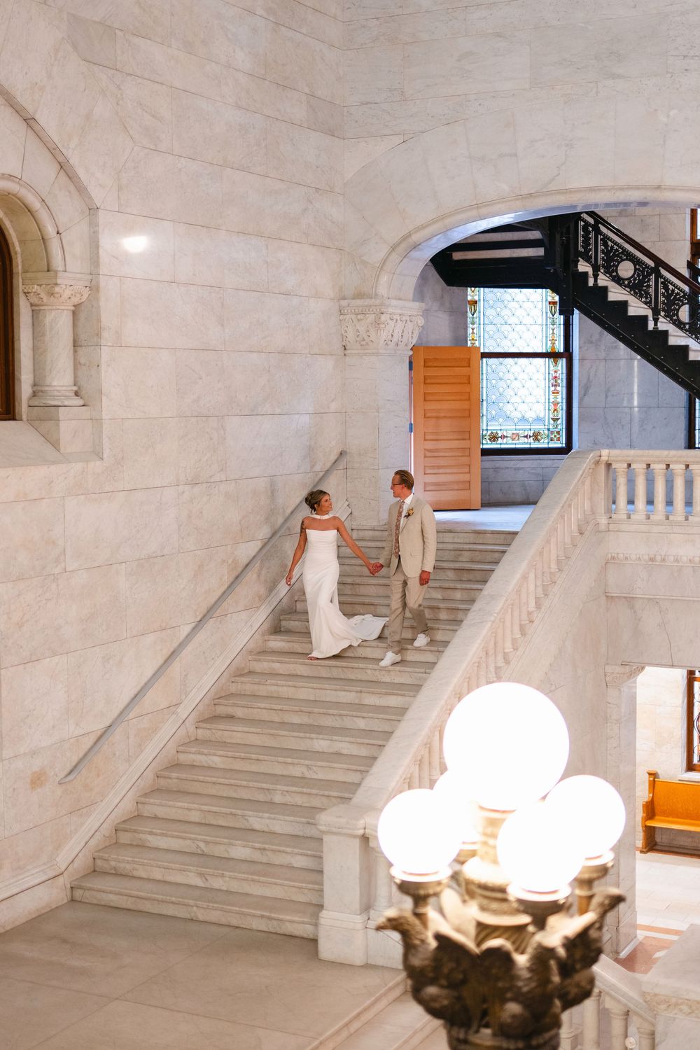 Elegant marble staircase in historic building interior with ornate white balustrades and globe light fixtures.