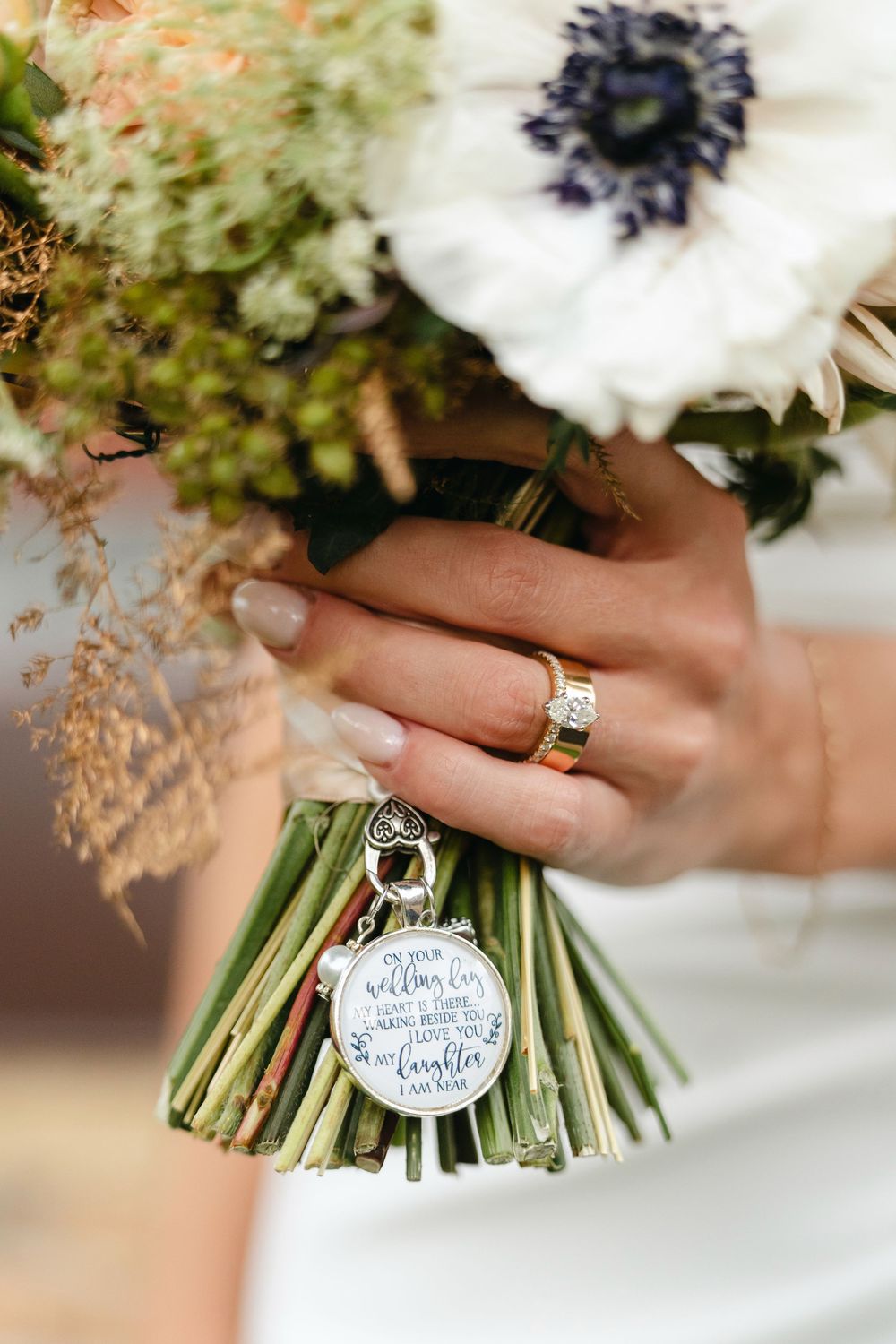 Wedding bouquet with white flowers and greenery features a decorative round tag charm tied with ribbon.