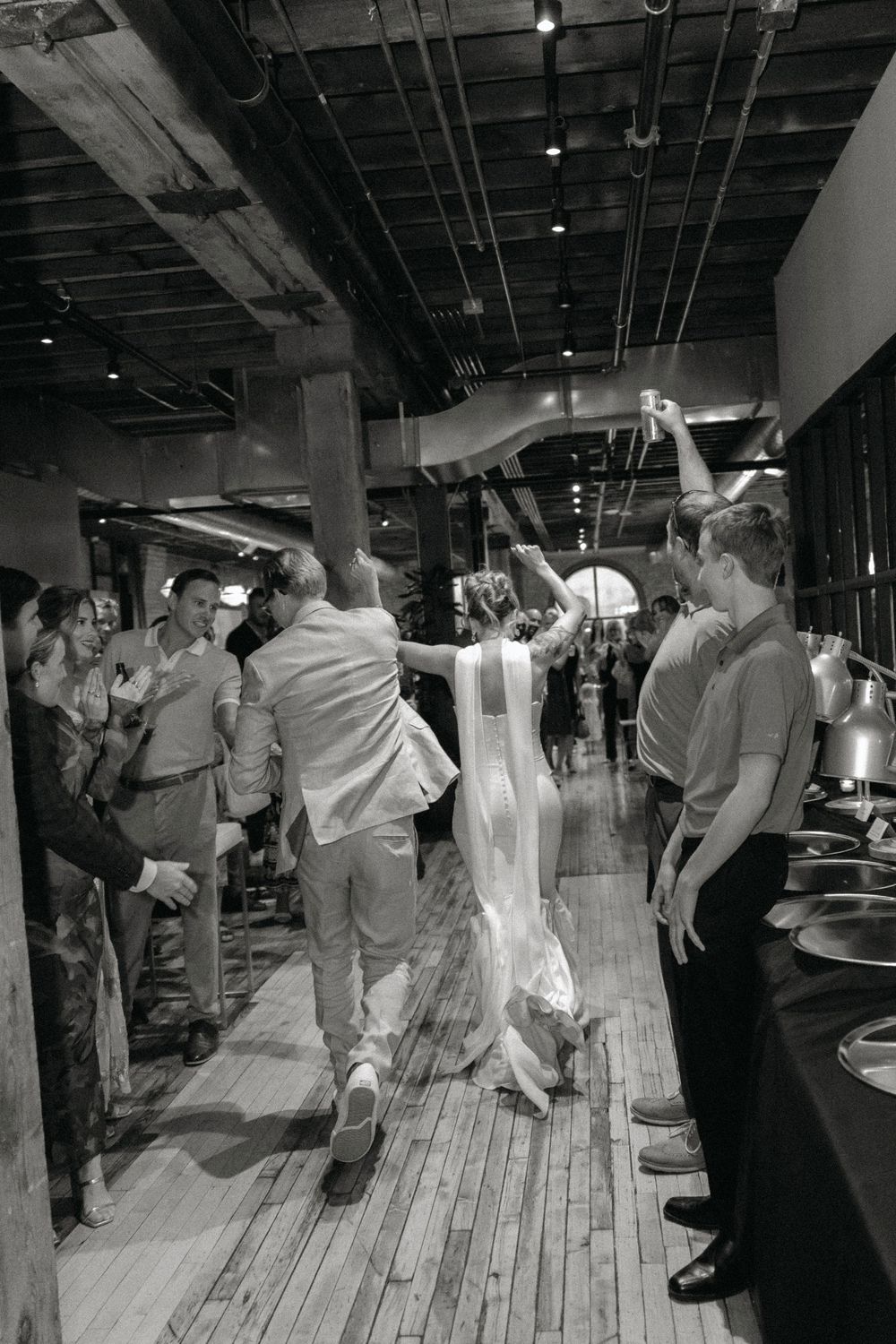 Couples dance together in a rustic venue with exposed wooden floors and industrial ceiling.