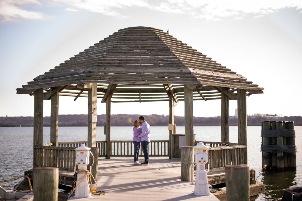 Couple enjoying sunset view from wooden gazebo on waterfront pier.