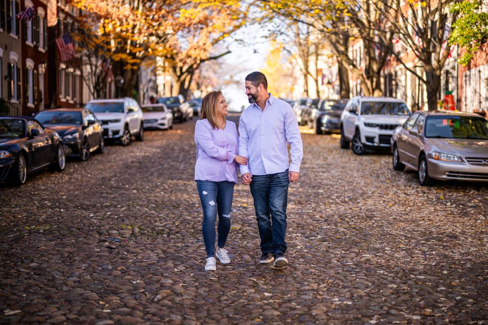 Couple walking together on leaf-covered street during fall season.