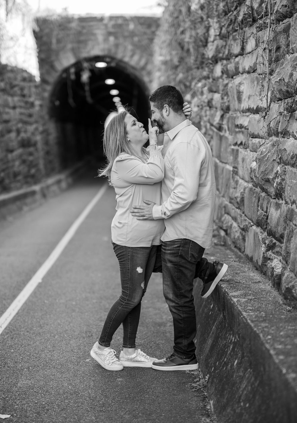 Black and white photo of romantic couple embracing in stone tunnel pathway.
