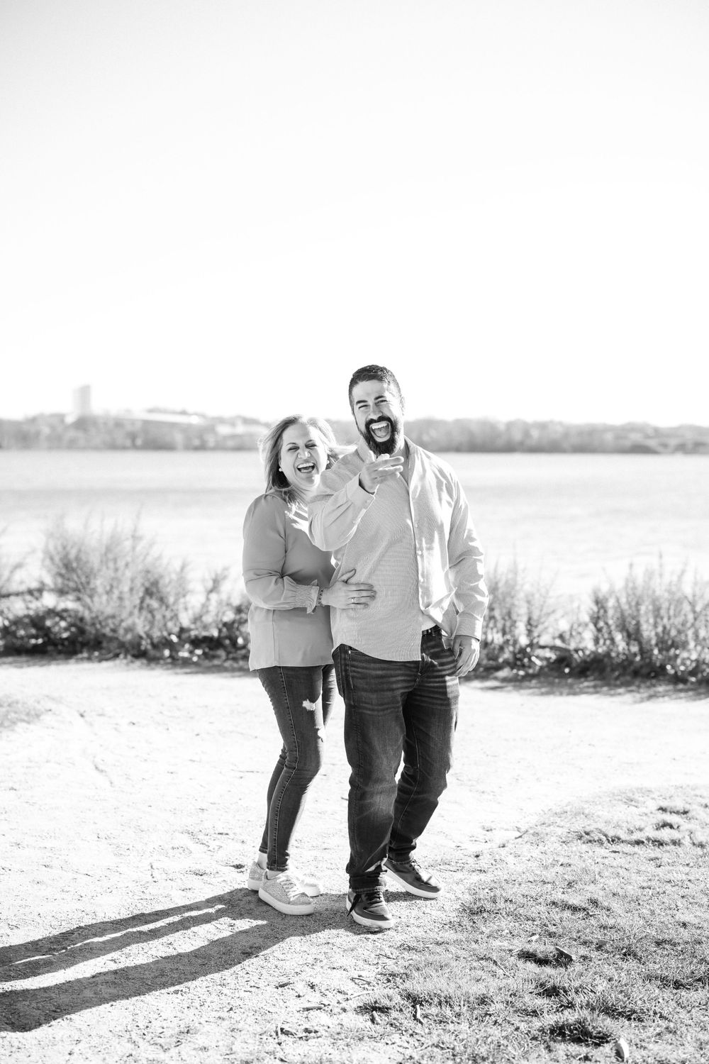 Black and white portrait of happy couple laughing together by waterfront.