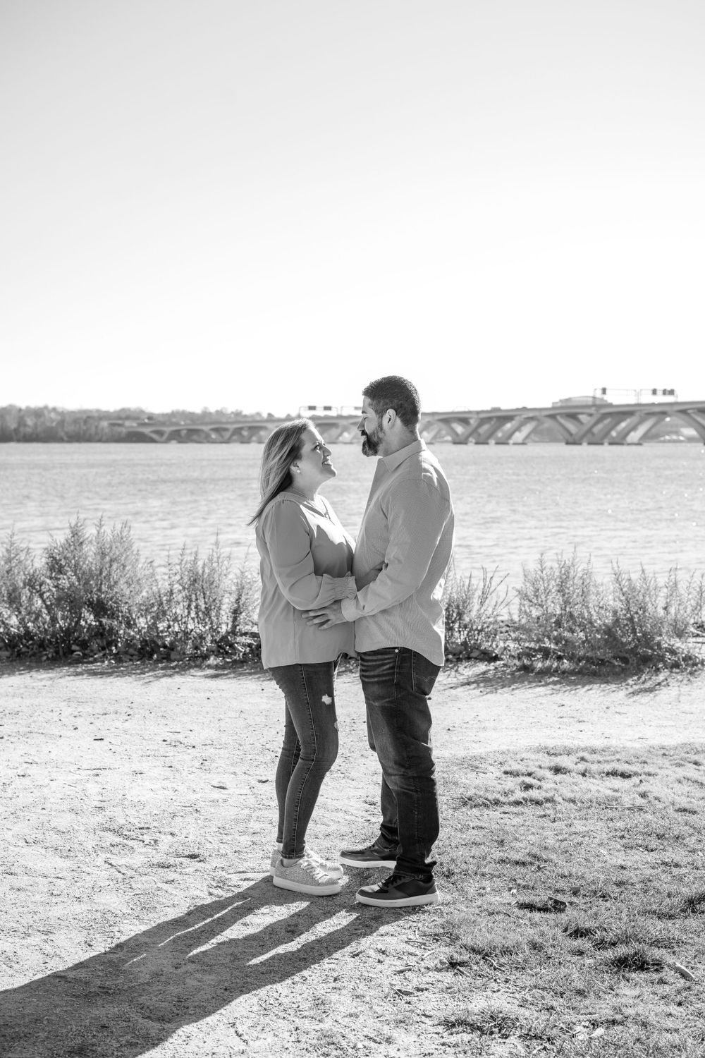Couple in casual wear embracing by waterfront on sunny day.