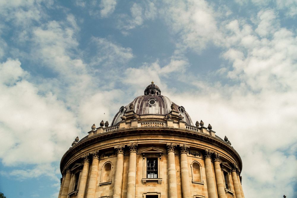 Low angle view of the ornate Radcliffe Camera dome against a cloudy blue sky in Oxford.