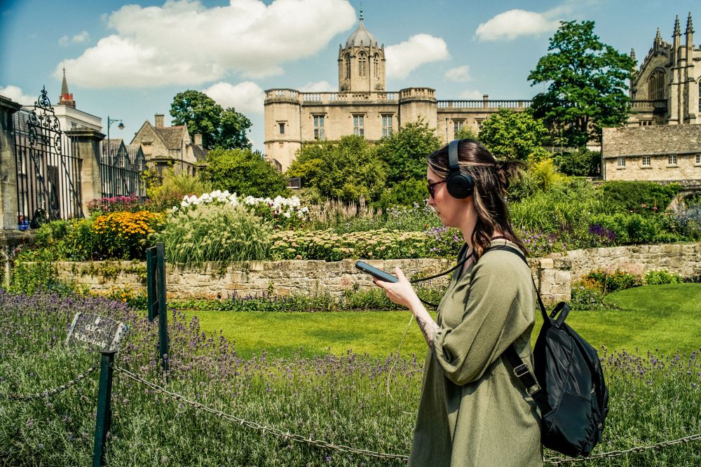 Tourist taking photos of Oxford University buildings across a flowering garden.