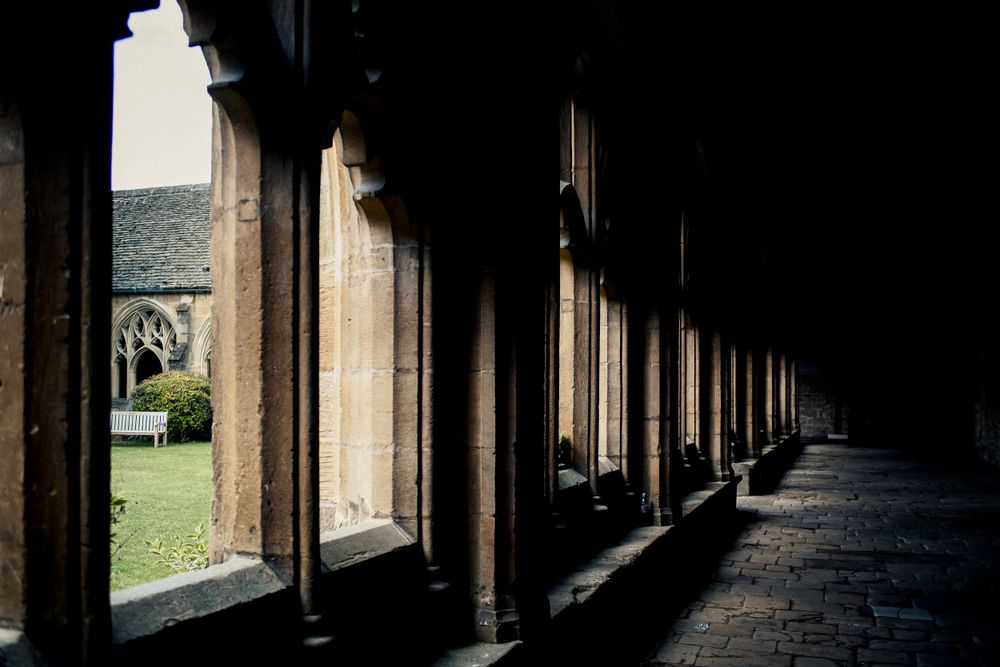Dark stone corridor with arched columns casting shadows in a historic Oxford building.