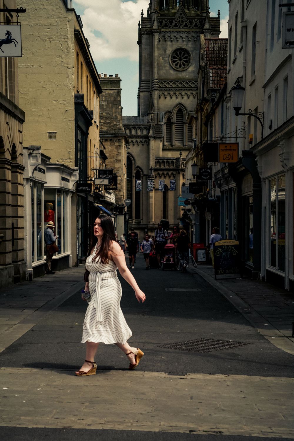 Historic city street leading to a grand cathedral tower with shops and buildings lining the pathway.