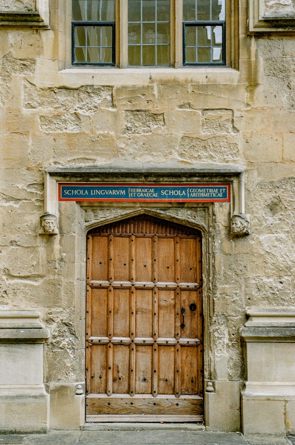 Ornate wooden door with stone archway and academic signage in historic Bath architecture.