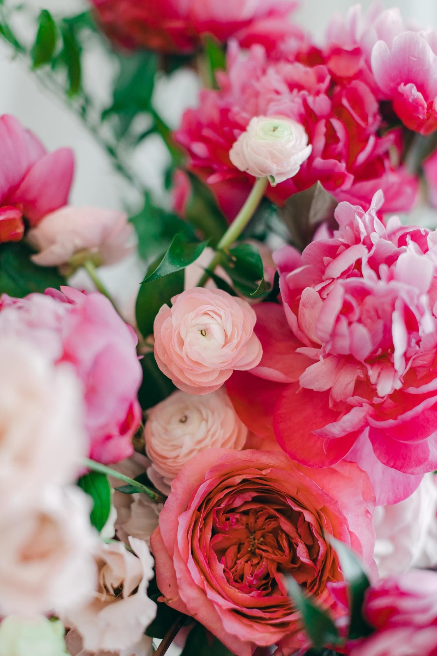 Close-up of pink peonies, ranunculus, and garden roses in a romantic floral arrangement with soft focus.