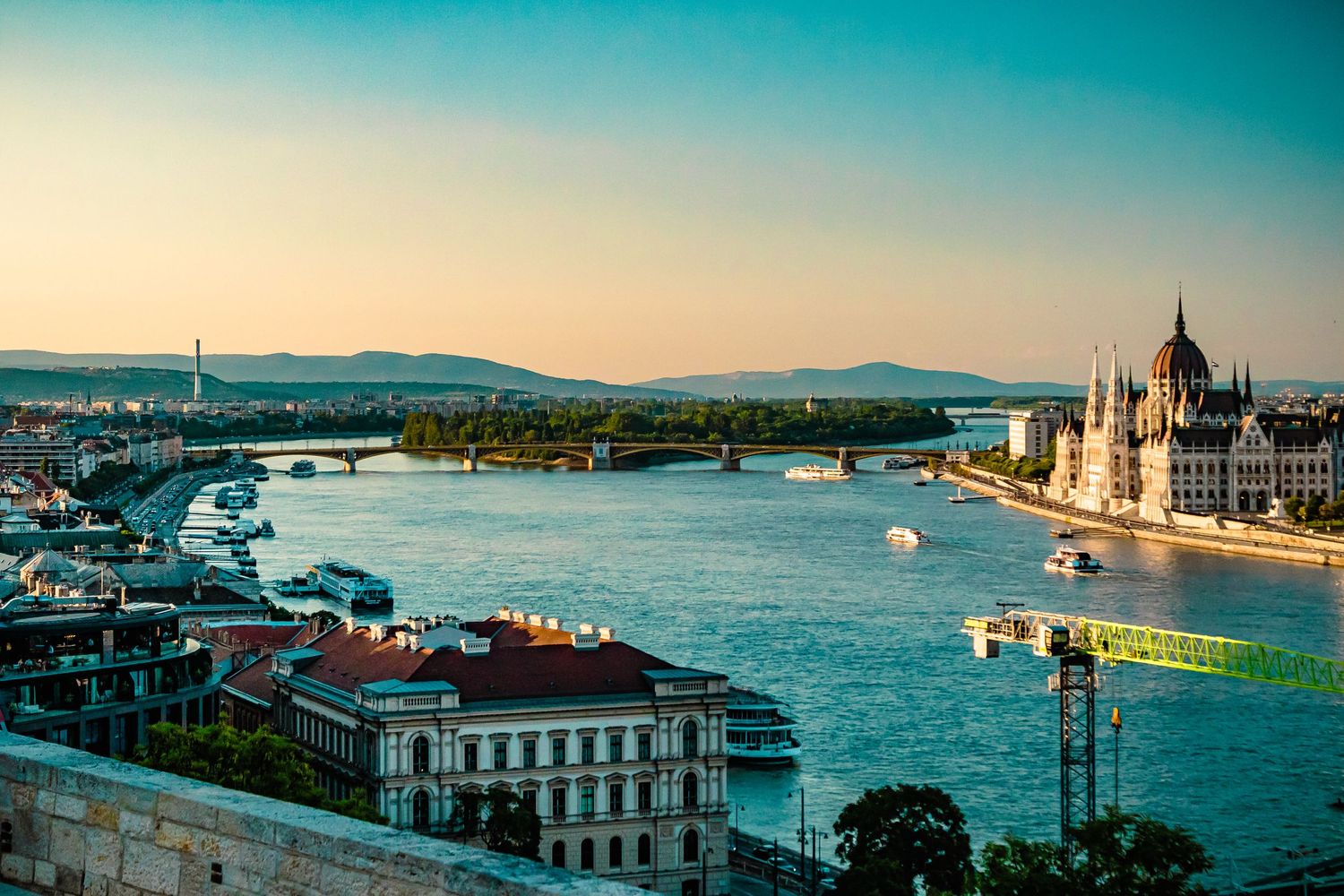 Budapest Parliament building and Danube River at sunset with boats and bridges visible.