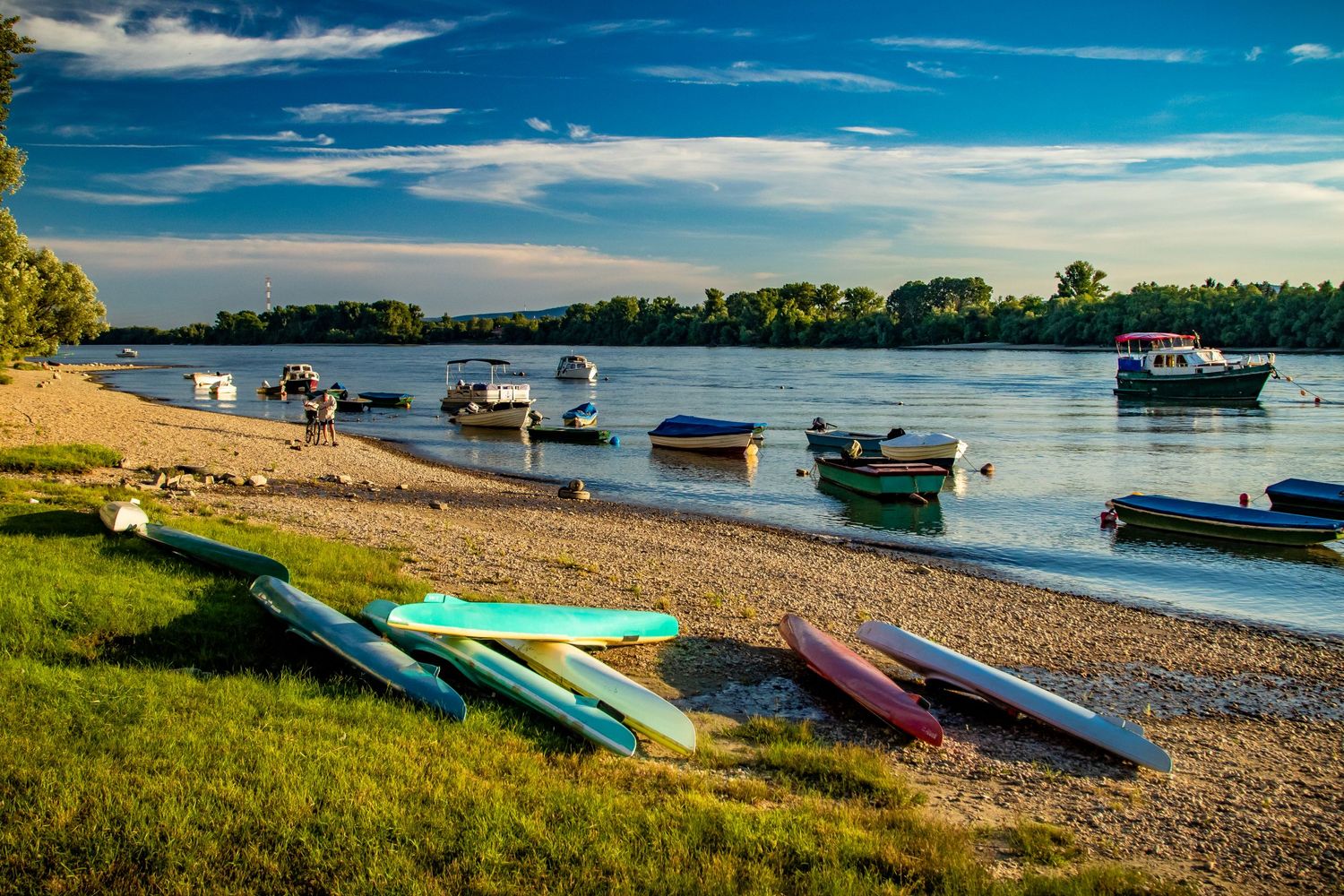 Colorful kayaks line a beach shore with boats anchored in the calm water beyond.